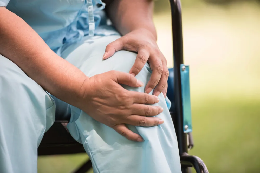 A person seated in a wheelchair holding their knee with both hands